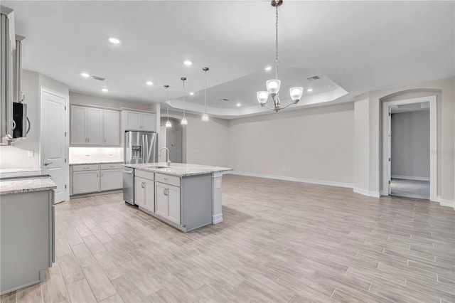 kitchen featuring gray cabinetry, sink, decorative light fixtures, a center island with sink, and appliances with stainless steel finishes