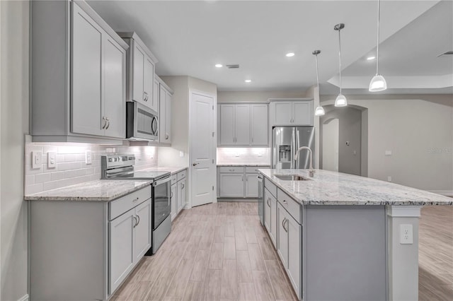 kitchen featuring stainless steel appliances, sink, decorative light fixtures, light hardwood / wood-style floors, and an island with sink