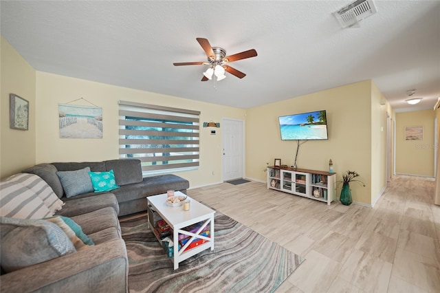 living room featuring ceiling fan, light wood-type flooring, and a textured ceiling