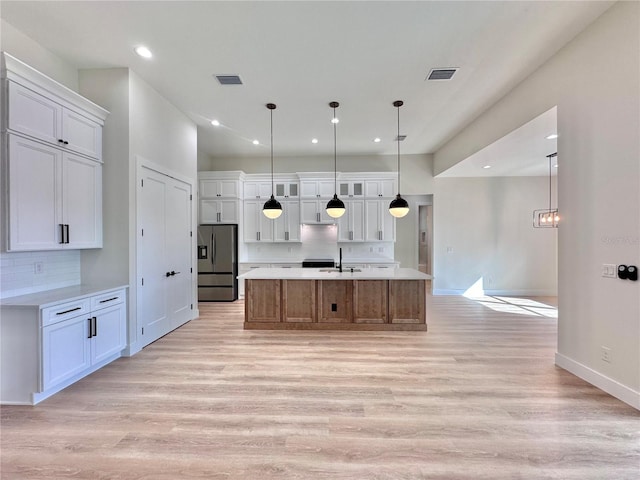 kitchen featuring white cabinets, stainless steel fridge with ice dispenser, hanging light fixtures, and an island with sink