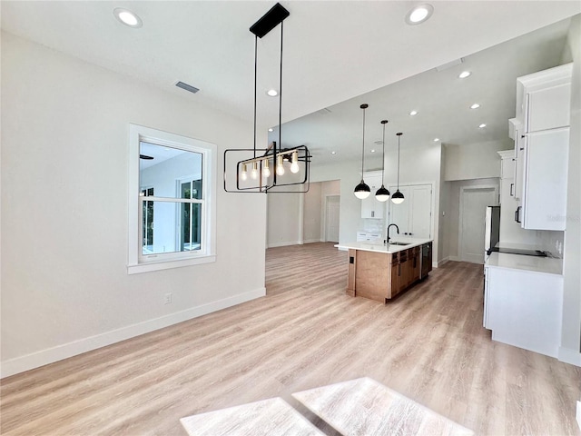 kitchen with sink, pendant lighting, light hardwood / wood-style flooring, white cabinetry, and an island with sink