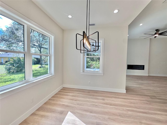 unfurnished dining area featuring ceiling fan with notable chandelier and light wood-type flooring