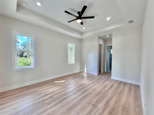 spare room with a raised ceiling, light hardwood / wood-style flooring, and ceiling fan