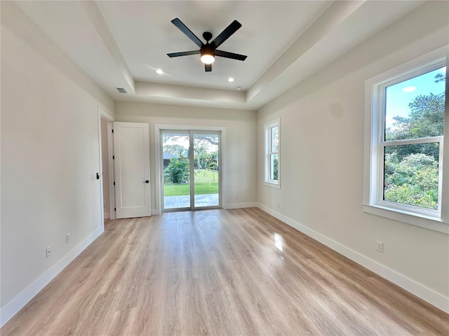 unfurnished room featuring a tray ceiling, light hardwood / wood-style flooring, ceiling fan, and a healthy amount of sunlight