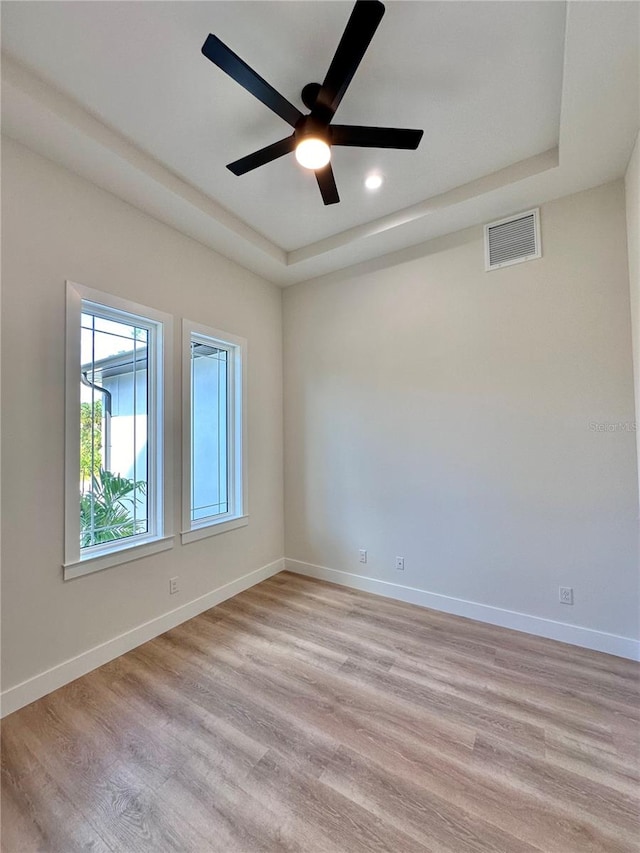 empty room featuring light wood-type flooring, a tray ceiling, and ceiling fan