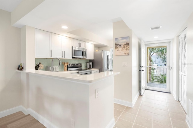 kitchen featuring backsplash, white cabinets, sink, kitchen peninsula, and stainless steel appliances