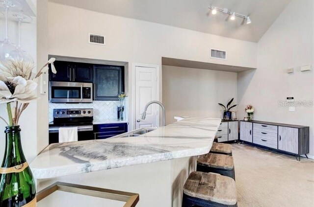 kitchen featuring sink, light stone counters, appliances with stainless steel finishes, tasteful backsplash, and a kitchen bar