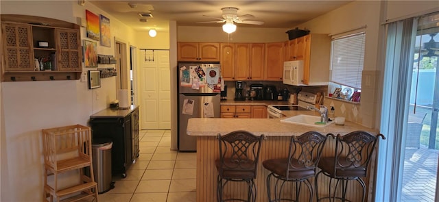 kitchen featuring light tile patterned flooring, sink, a breakfast bar area, kitchen peninsula, and white appliances