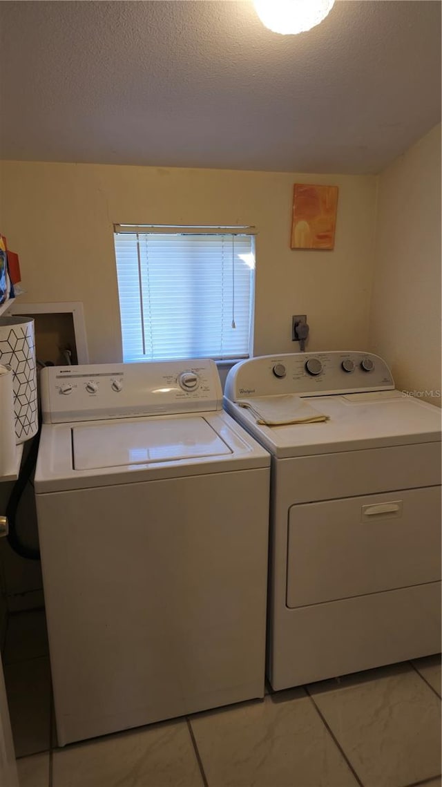 laundry room featuring washer and dryer, a textured ceiling, and light tile patterned flooring