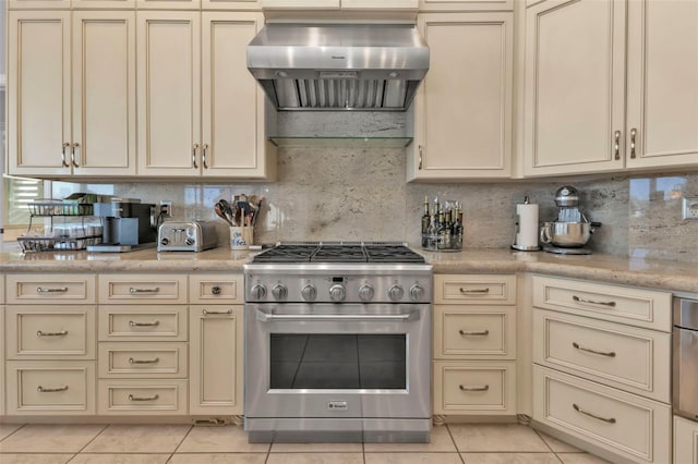 kitchen featuring high end range, wall chimney exhaust hood, light tile patterned floors, and cream cabinetry