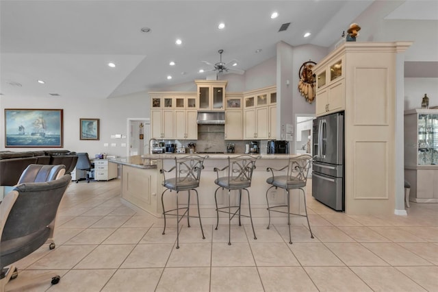 kitchen with ventilation hood, ceiling fan, stainless steel fridge, an island with sink, and a kitchen bar