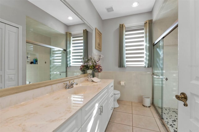 bathroom with tile patterned floors, vanity, tile walls, toilet, and a shower with shower door