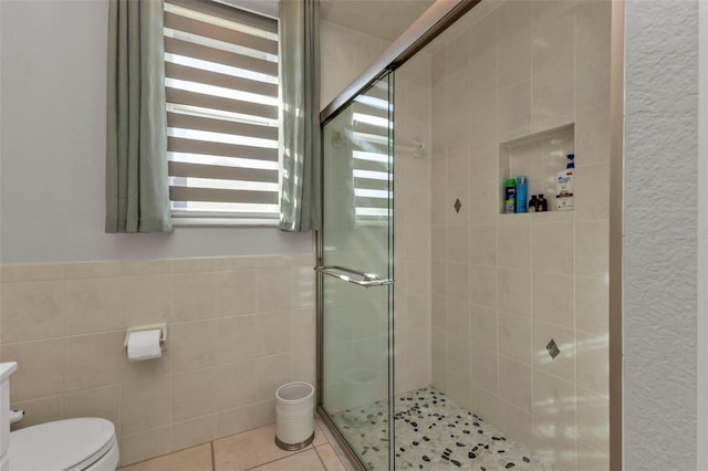 bathroom with tile patterned flooring, toilet, a shower with door, and tile walls