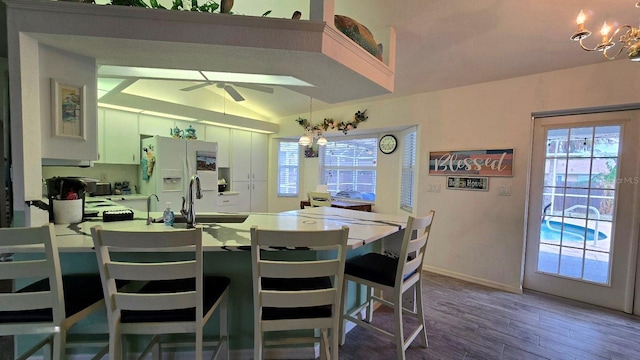 kitchen featuring white refrigerator with ice dispenser, vaulted ceiling, white cabinets, ceiling fan with notable chandelier, and hardwood / wood-style flooring