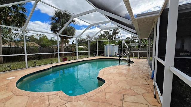 view of pool with glass enclosure, a shed, and a patio