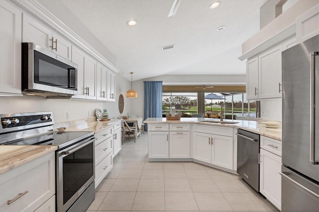 kitchen with lofted ceiling, sink, appliances with stainless steel finishes, decorative light fixtures, and white cabinetry