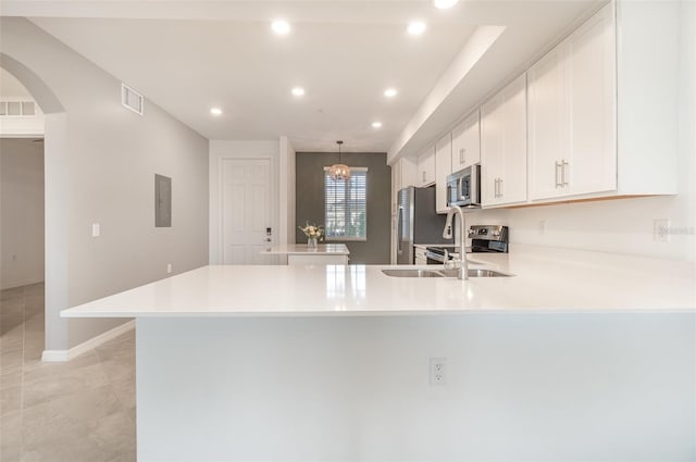 kitchen with kitchen peninsula, appliances with stainless steel finishes, decorative light fixtures, a chandelier, and white cabinetry