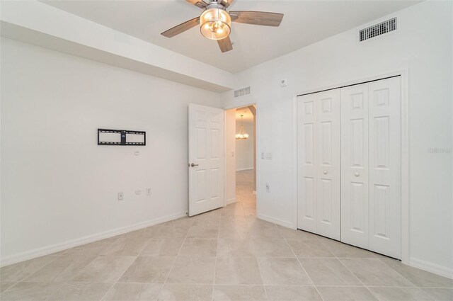 unfurnished bedroom featuring ceiling fan with notable chandelier, light tile patterned floors, and a closet