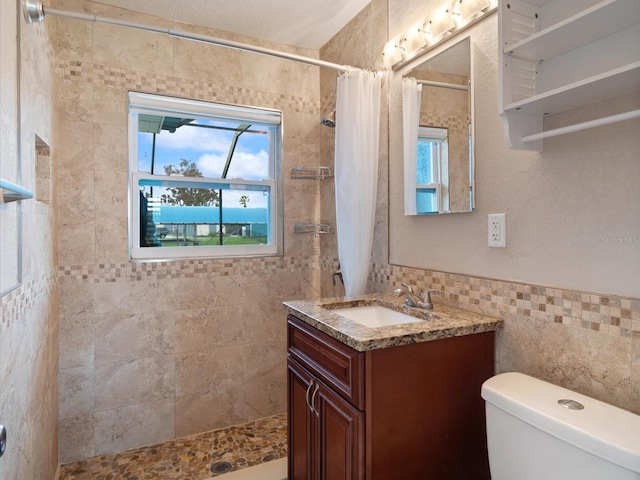 bathroom with a shower with shower curtain, vanity, toilet, and tile walls