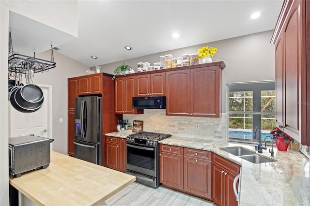 kitchen featuring sink, appliances with stainless steel finishes, tasteful backsplash, light hardwood / wood-style floors, and light stone counters