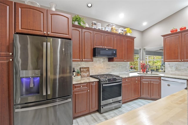 kitchen featuring appliances with stainless steel finishes, light wood-type flooring, vaulted ceiling, sink, and butcher block countertops