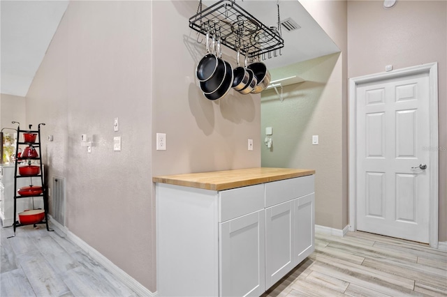 bar featuring light wood-type flooring, butcher block countertops, and white cabinetry