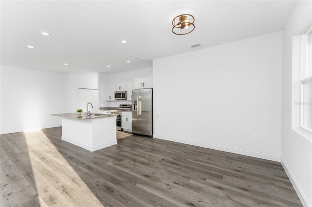 kitchen with light stone countertops, white cabinets, dark hardwood / wood-style flooring, stainless steel appliances, and a kitchen island with sink