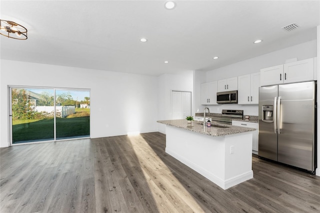 kitchen with appliances with stainless steel finishes, white cabinetry, light stone counters, dark hardwood / wood-style floors, and an island with sink