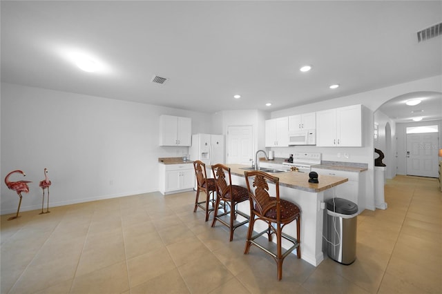 kitchen with sink, an island with sink, white appliances, a breakfast bar, and white cabinets