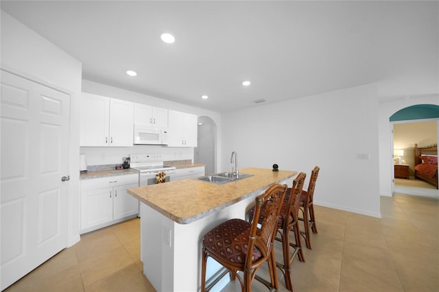 kitchen with a kitchen bar, white appliances, sink, white cabinets, and an island with sink