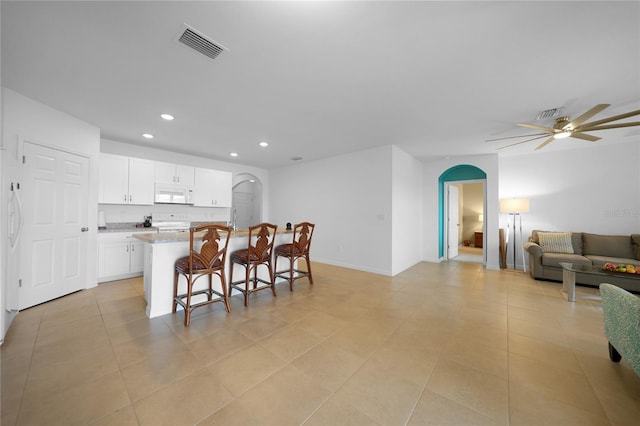 kitchen with white appliances, white cabinets, ceiling fan, light stone countertops, and a breakfast bar area