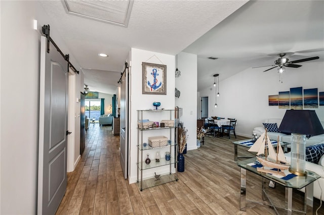 hall featuring hardwood / wood-style floors, a barn door, a textured ceiling, and lofted ceiling