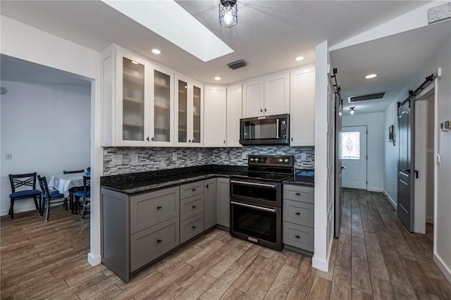 kitchen featuring white cabinets, a barn door, wood-type flooring, and stainless steel range with electric cooktop