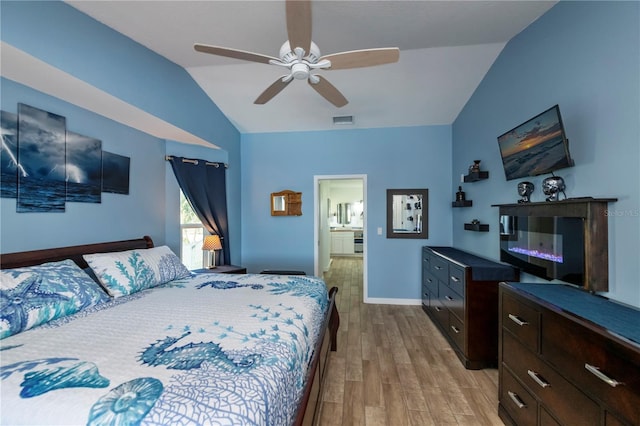 bedroom featuring connected bathroom, ceiling fan, light hardwood / wood-style flooring, and vaulted ceiling