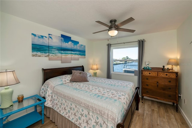 bedroom with hardwood / wood-style floors, ceiling fan, and a water view