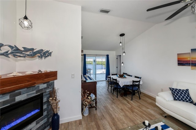 living area featuring wood finished floors, visible vents, baseboards, vaulted ceiling, and a glass covered fireplace