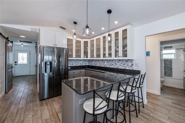 kitchen with a barn door, glass insert cabinets, white cabinetry, stainless steel fridge with ice dispenser, and decorative light fixtures