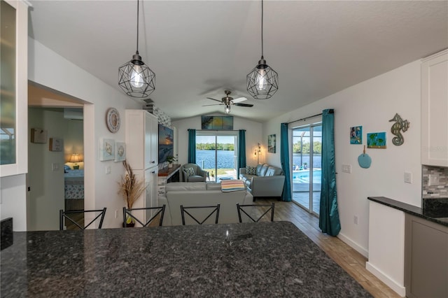 dining room featuring light wood finished floors, baseboards, lofted ceiling, ceiling fan, and an AC wall unit