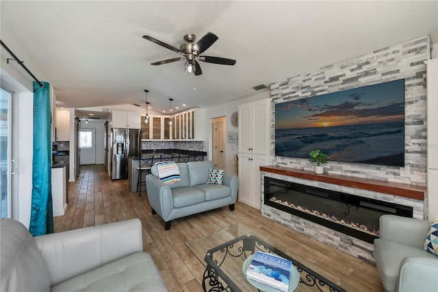 living area with lofted ceiling, a fireplace, visible vents, a ceiling fan, and light wood-style floors