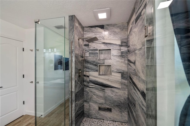 full bathroom with visible vents, a shower stall, a textured ceiling, and wood finished floors