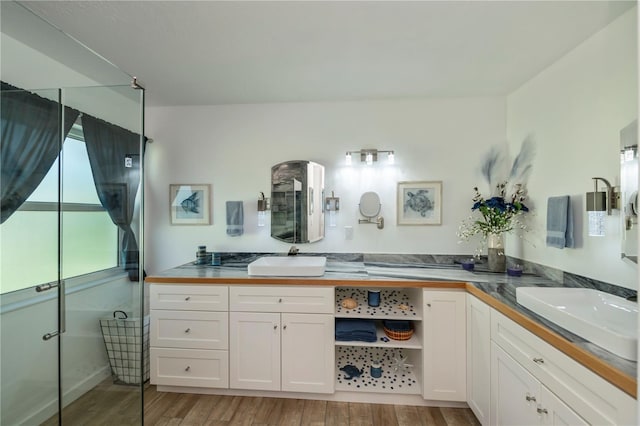 full bath featuring wood finished floors, a shower with door, a sink, and double vanity