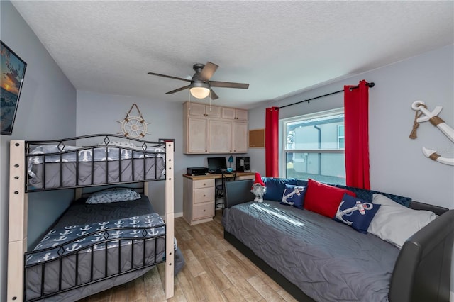 bedroom featuring a textured ceiling, light wood finished floors, built in desk, and a ceiling fan