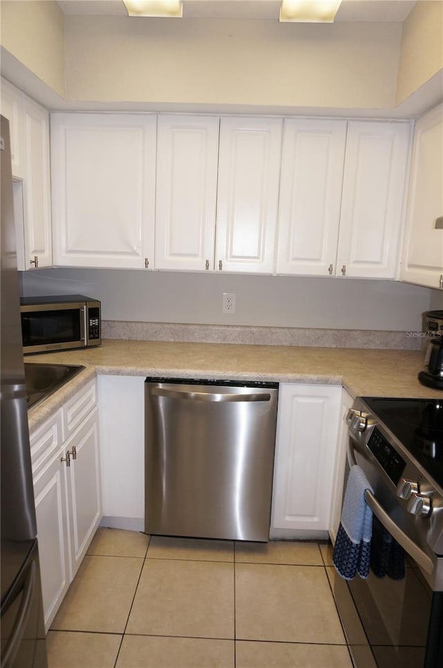 kitchen featuring appliances with stainless steel finishes, light tile patterned floors, and white cabinetry