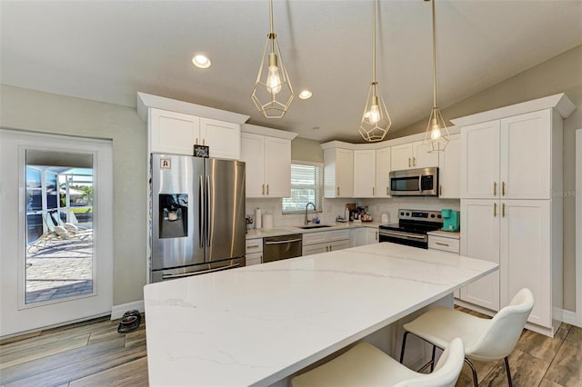 kitchen featuring sink, stainless steel appliances, decorative light fixtures, white cabinets, and light wood-type flooring