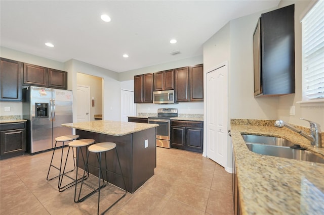 kitchen with appliances with stainless steel finishes, sink, a breakfast bar area, a center island, and light stone countertops