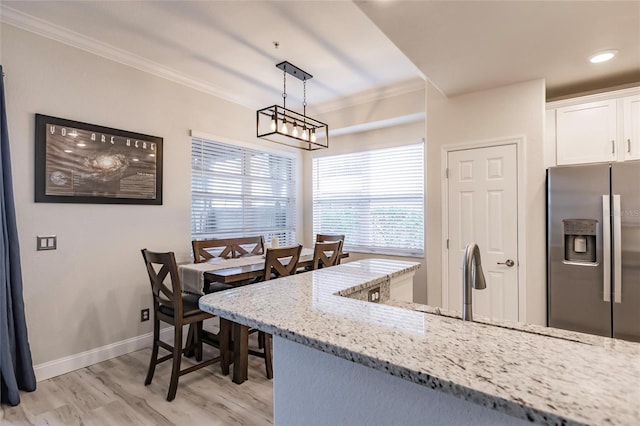 kitchen with white cabinets, crown molding, stainless steel fridge, light wood-type flooring, and light stone counters