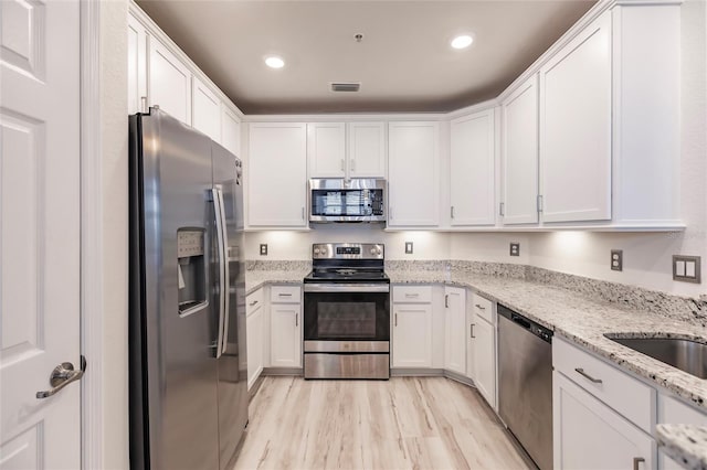 kitchen featuring light stone countertops, white cabinets, light hardwood / wood-style floors, and appliances with stainless steel finishes