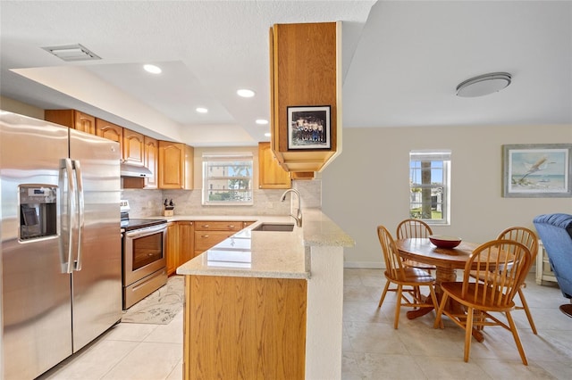 kitchen featuring sink, appliances with stainless steel finishes, tasteful backsplash, light stone counters, and kitchen peninsula