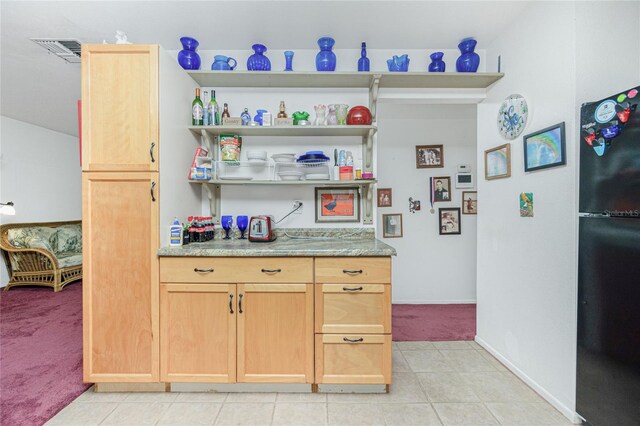 bar with light brown cabinets, black refrigerator, and light tile patterned floors