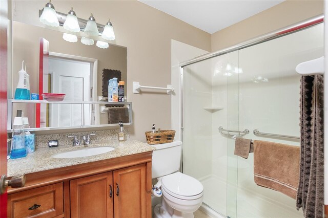 bathroom featuring a shower with door, vanity, and toilet